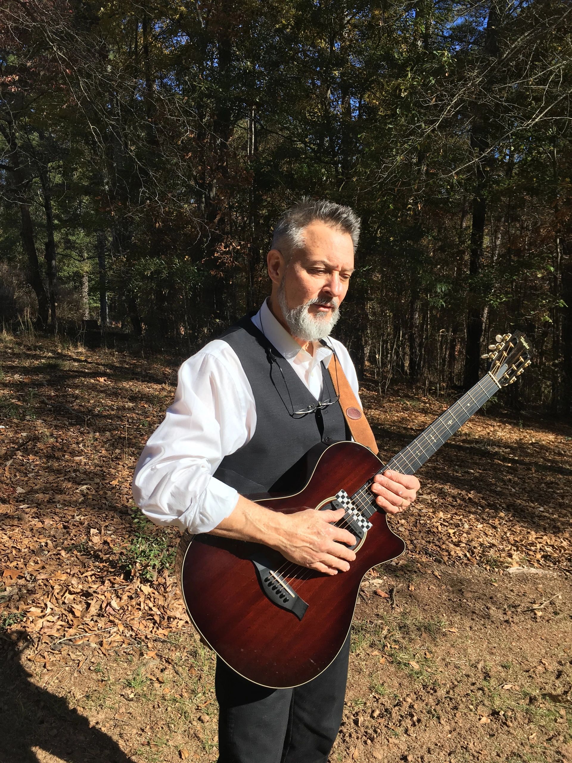 Craig Gleason playing acoustic guitar in a forest